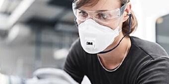 Persoon met veiligheidsbril en stofmasker
