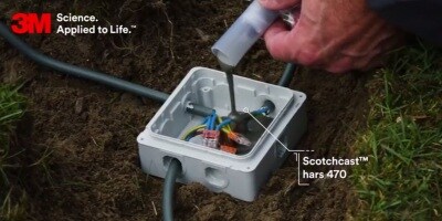 Een man brengt zwarte 3M tape aan om een elektrische kabelmantel te repareren.
