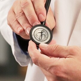 Close-up van een arts die het borststuk van een 3M Littmann Stethoscoop met een Littmann zegel op het membraan vasthoudt.