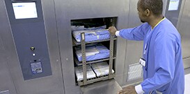 Een medewerker van de sterilisatieafdeling duwt de instrumententrolley in de sterilisator
