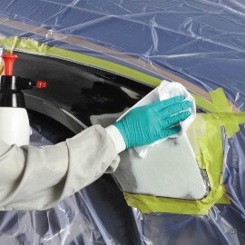 Een hand met een groene handschoen die de carrosserie van een auto ontvet met een wit doekje