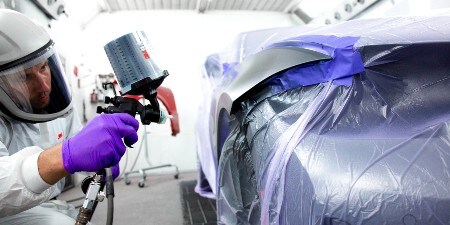 mannelijke spuiter die op een auto spuit met een 3M-spuitpistoolsysteem
