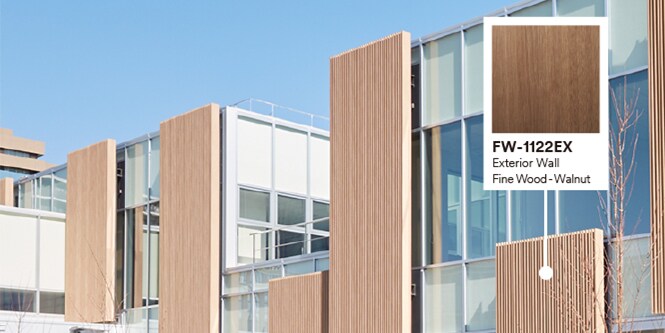 Buitenkant van gebouw met glazen en houten gevel met productaanduiding van notenhouten DINOC-exterieurfolie.
