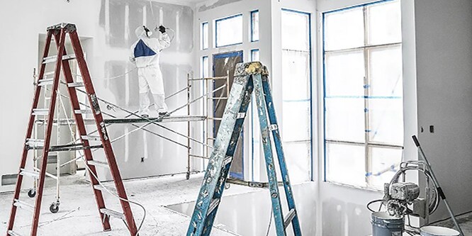Professionele decorateur die boven op een ladder staat en muren schildert
