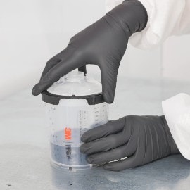 Handen met donkergrijze handschoenen die de primer mengen met een 3M-spuitbeker