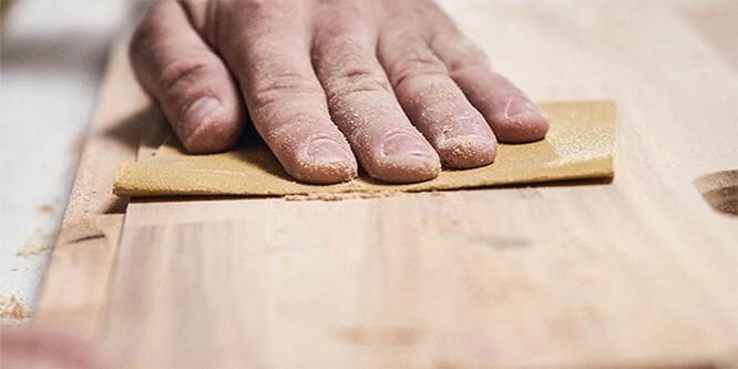 Handen die 3M Geavanceerde Schuurmiddelen gebruiken om een tafel van hout te schuren

