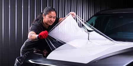 Wrap-installateur die folie op de motorkap van een auto aanbrengt.
