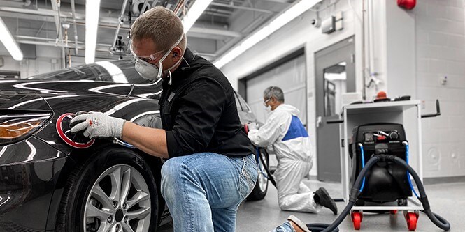 Afbeelding toont een man die hoogwaardige schuurmiddelen en gereedschappen gebruikt op een auto om uitstekende resultaten te bereiken.
