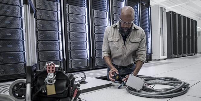 een werknemer in een datacenter installeert elektrische leidingen onder de vloer
