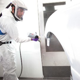 Mannelijke spuiter die een wit carrosseriedeel spuit met behulp van een 3M-spuitsysteem