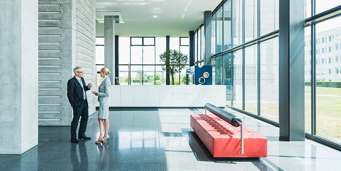 Beeld van een kantoorgebouwlobby met glazen wanden, met twee zakenmensen in gesprek
