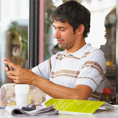 Afbeelding van een man die aan tafel naar zijn mobiele apparaat kijkt
