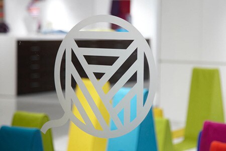 Helder raam met een logo in lijn in geëtst glasstijl met kleurrijke vormen erachter.
