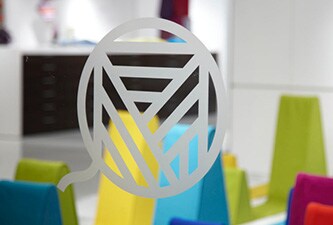 Helder raam met een logo in lijn in geëtst glasstijl met kleurrijke vormen erachter.
