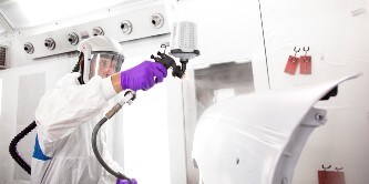 Mannelijke spuiter die primer op een deel van een auto spuit met het 3M Performance spuitpistool
