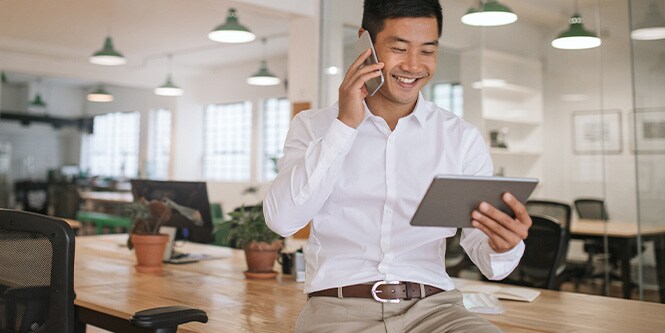 Afbeelding van een lachende zakenman die aan de telefoon praat en naar een tablet kijkt.

