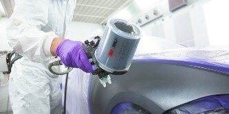 mannelijke spuiter die lak op een deel van een auto spuit met het 3M performance spuitpistool
