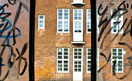 Drieruitsraam met zicht op bakstenen gebouw. Zijruiten met graffiti, middenruit is schoon
