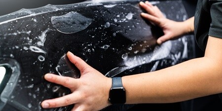 Persoon die verfbeschermingsfolie op een auto aanbrengt
