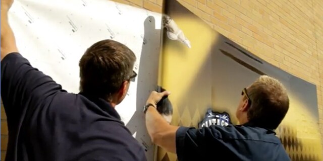Twee mannen plaatsen witte 3M Controltac printfolie op muur